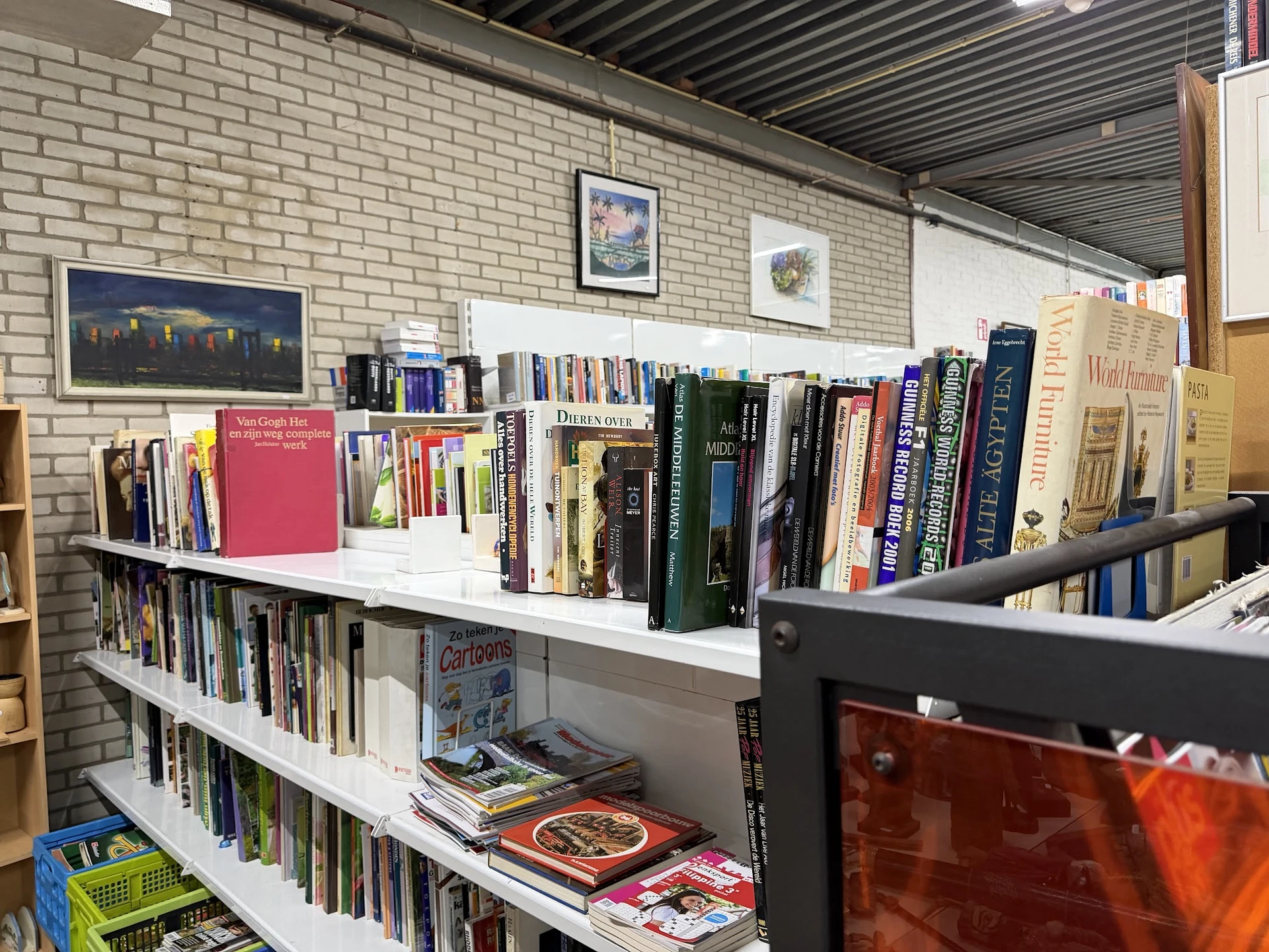 Boeken- en mediarekken met tweedehands boeken, dvd's en cd's op witte stellingen tegen bakstenen muur
