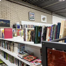 Boeken- en mediarekken met tweedehands boeken, dvd's en cd's op witte stellingen tegen bakstenen muur