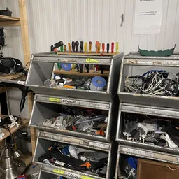 Metalen opbergbakken gevuld met gereedschap, elektrische kabels en diverse huishoudelijke artikelen