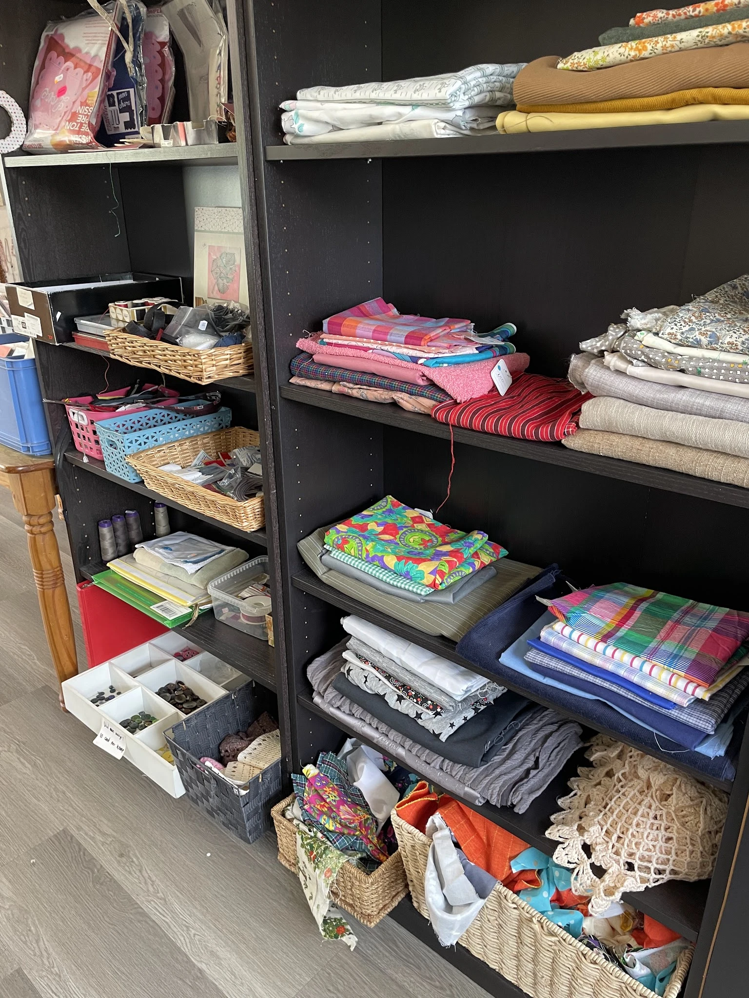 Zwarte stellingen met stapels textiel en huishoudtextiel, waaronder bedlinnen, handdoeken en kussens in verschillende kleuren