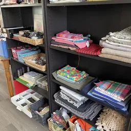 Zwarte stellingen met stapels textiel en huishoudtextiel, waaronder bedlinnen, handdoeken en kussens in verschillende kleuren