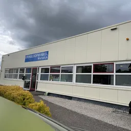 Witte gevel van kringloopwinkel Marsdijk met grote ramen, blauwe winkelnaambord en ingang, fiets ernaast