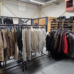 Rekken met tweedehands kleding, vooral jassen en truien in verschillende kleuren en maten.