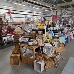 Uitgestalde huishoudelijke artikelen en meubilair, waaronder rotan manden, stoelen en diverse huisraad in een kringloopwinkel