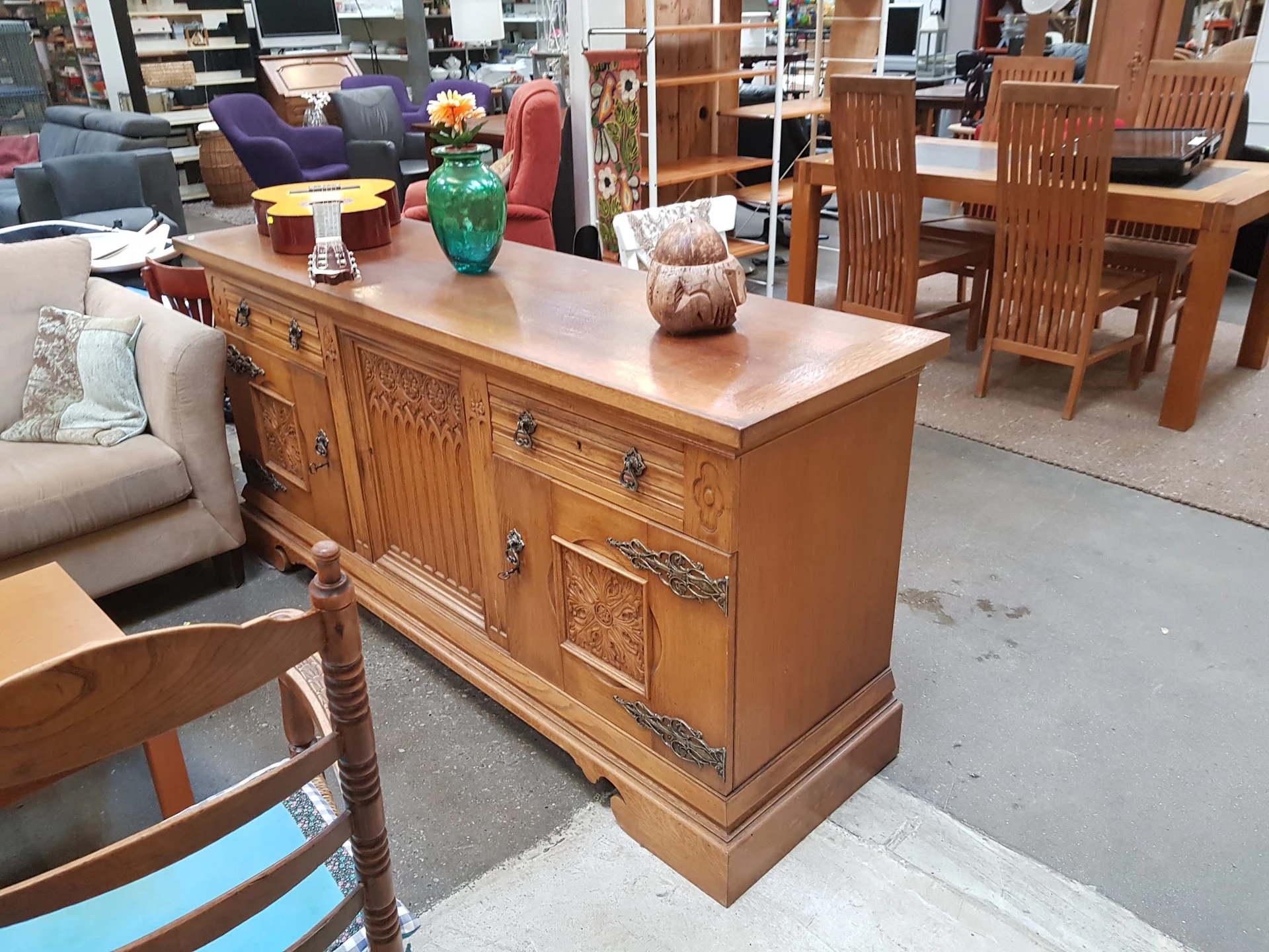 Houten dressoir met beschilderde deuren en laden, opgesteld in een kringloopwinkel tussen ander meubilair