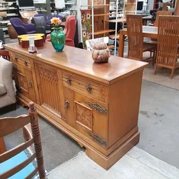 Houten dressoir met beschilderde deuren en laden, opgesteld in een kringloopwinkel tussen ander meubilair