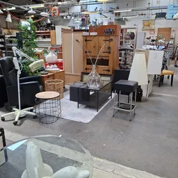 Winkelvloer met uitgestalde meubels en huishoudartikelen, waaronder zwarte zitbanken, tafels, stoelen en decoratieve items.