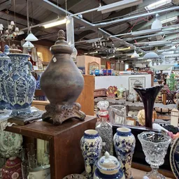 Uitgestalde antieke en decoratieve objecten: bruine urn, blauwe porseleinen vazen, glazen voorwerpen en andere huishoudelijke