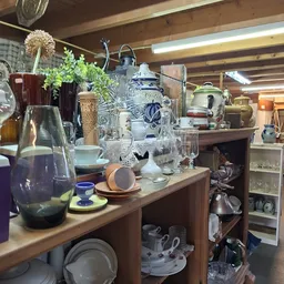 Uitgestalde huishoudelijke artikelen en decoratieve items op houten toonbank en achtergrond, inclusief vazen, servies en kera