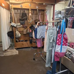 Rekken met tweedehands kleding, waaronder jeans, rokken en felgekleurde kledingstukken in de winkel