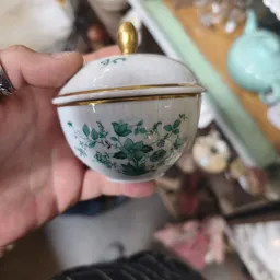 Close-up van een wit porselein dekselschaaltje met groen bloemenpatroon en gouden rand
