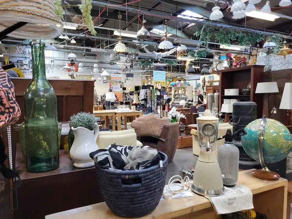 Binnenaanzicht van kringloopwinkel met uiteenlopende tweedehandsartikelen: meubels, decoratie, lampen, huisraad en textiel op