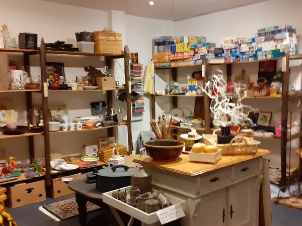 Winkelvloer met houten stellingen vol huishoudelijke artikelen, servies en decoratie; centrale houten tafel met kastje.