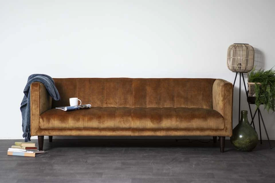 Bruinleren vintage bank met houten poten tegen witte muur, met accessoires ernaast