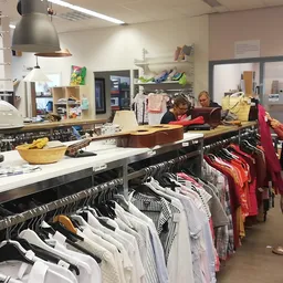 Winkelvloer met kledingrekken, klanten aan het winkelen, stellingen met spullen op de achtergrond