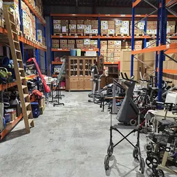 Binnenaanzicht kringloopwinkel met oranje en blauwe stellingen, dozen, fietsen en diverse spullen