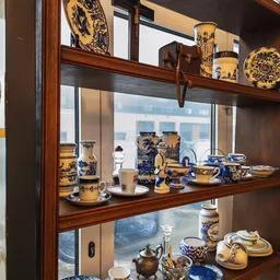 Glazen vitrinekast met antieke gele en blauwe porseleinen serviesgoed en decoratieve objecten