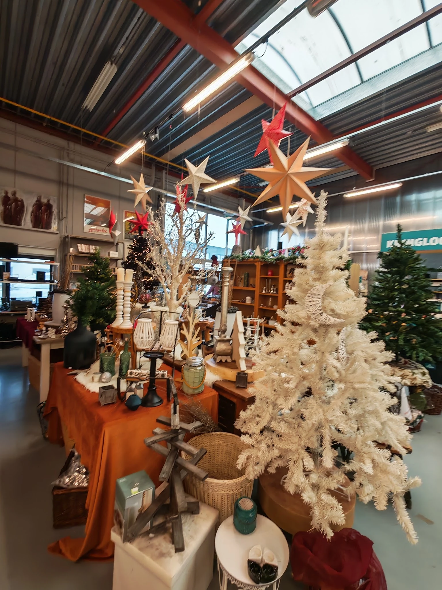 Kerstdecoratie uitgestald met witte kunstbomen, grote sterren en diverse huisraad op oranje tafels in de winkel