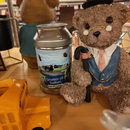 Bruine knuffelbeer in pak en stropdas naast een melkbus met opdruk 'Groeten uit Dalfsen'