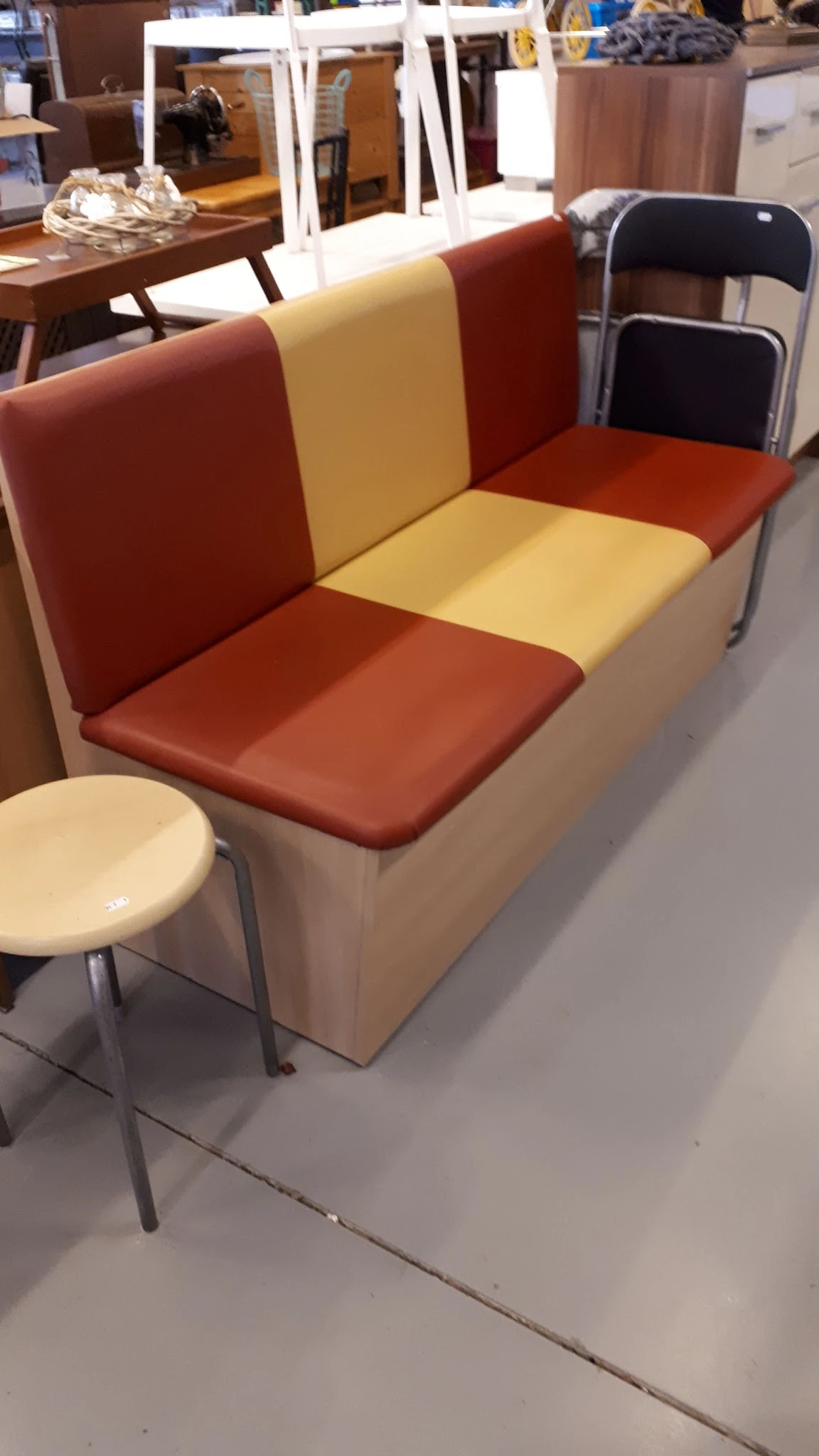 Bankje met rood en crème gekleurde bekleding en metalen poten, naast een klein rond krukje