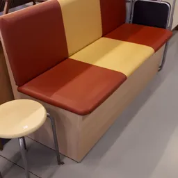 Bankje met rood en crème gekleurde bekleding en metalen poten, naast een klein rond krukje
