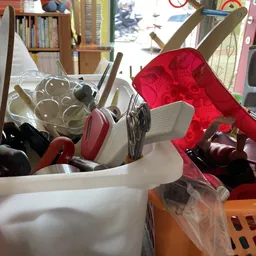 Diverse huishoudartikelen en keukengerei in bakken en manden, waaronder rode en witte plastic bakken met lepels, spatelset en