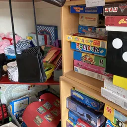 Houten stellingen met gestapelde bordspellen, speelgoed en ander tweedehands assortiment in een kringloopwinkel