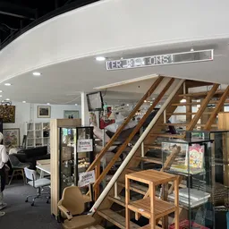 Winkelvloer met houten trap naar mezzanine, stellingen met spullen, witte plafond met verlichting