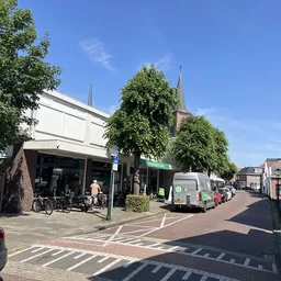 Straatgevel van kringloopwinkel met witte bovenbouw, bakstenen onderdeel, winkelruit en groene luifel