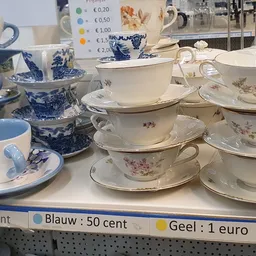 Uitgestalde serviesgoed met kopjes, schotels en kannen in blauw-wit en bloemenmotief met prijskaartjes