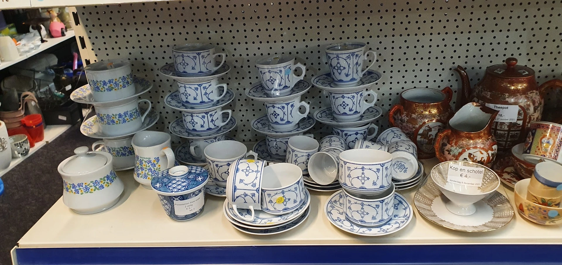 Uitgestalde serviesgoed met blauw-wit porselein kopjes, schotels en borden op een stellage