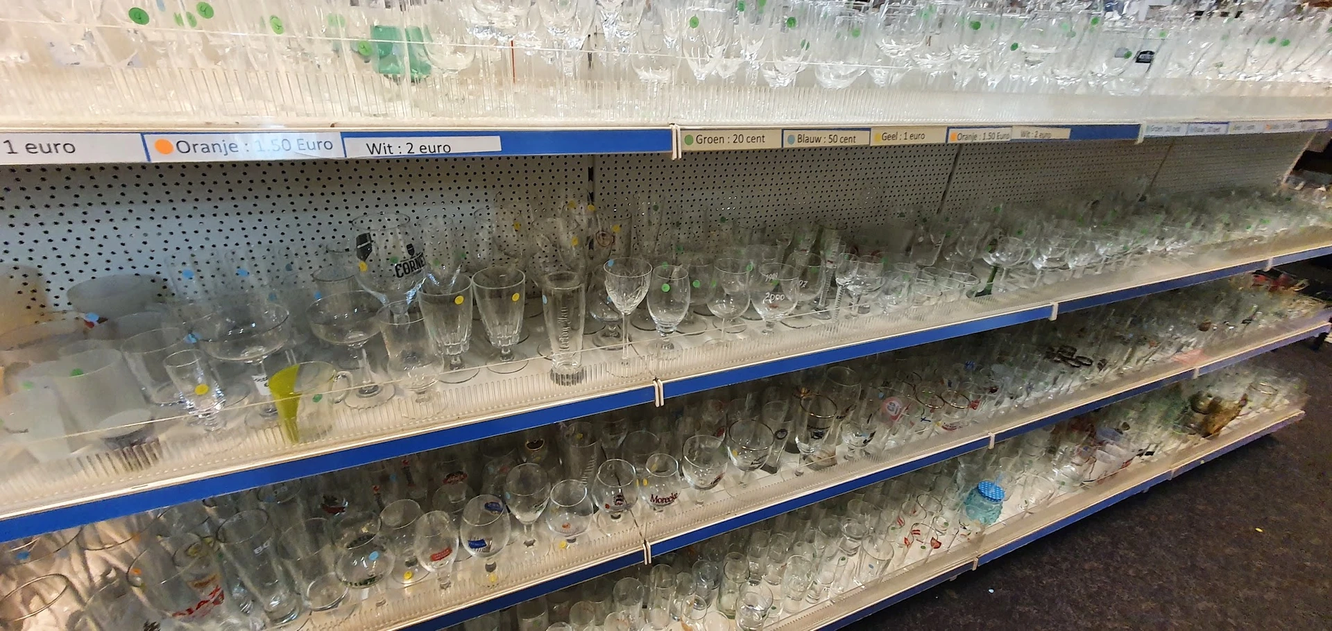 Glazen en bekers op drie schappen, verschillende formaten en stijlen, met prijskaartjes