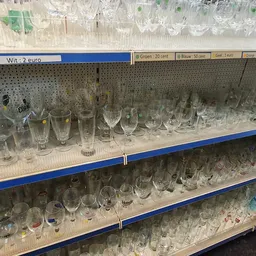 Glazen en bekers op drie schappen, verschillende formaten en stijlen, met prijskaartjes