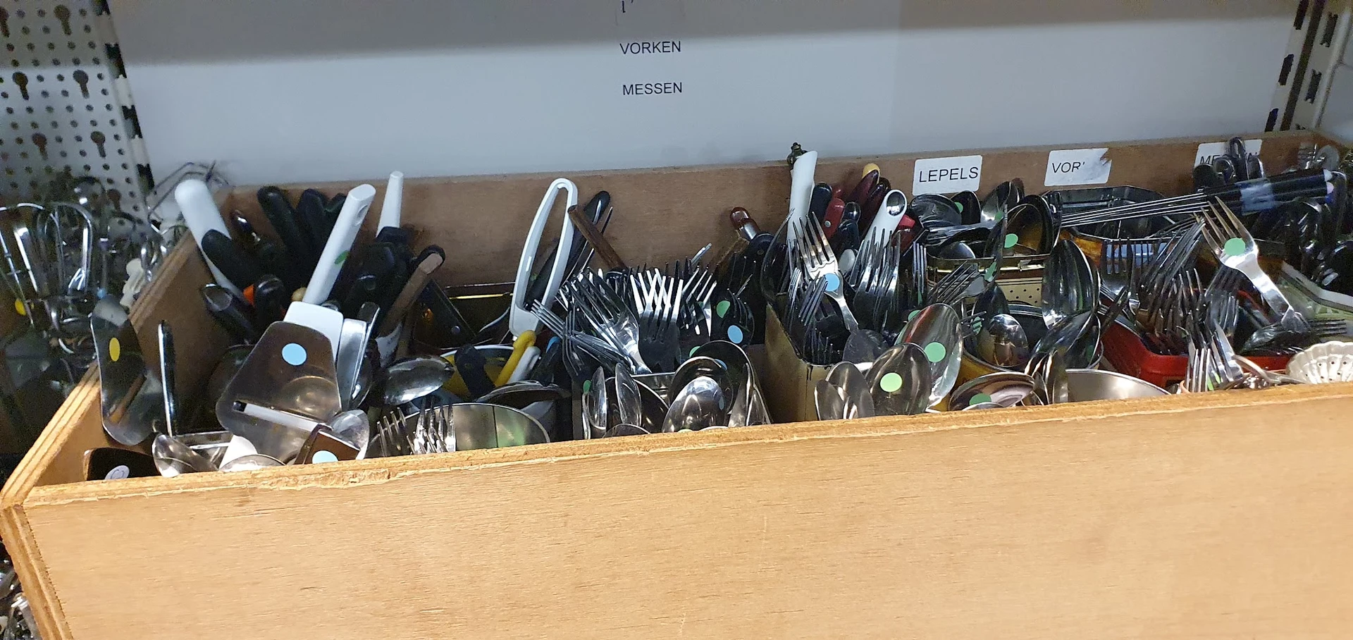 Houten kist met diverse bestek, keukengerei en servies in een kringloopwinkel