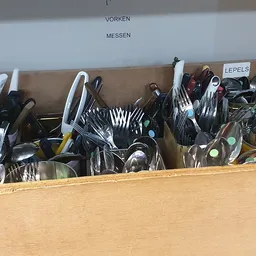 Houten kist met diverse bestek, keukengerei en servies in een kringloopwinkel