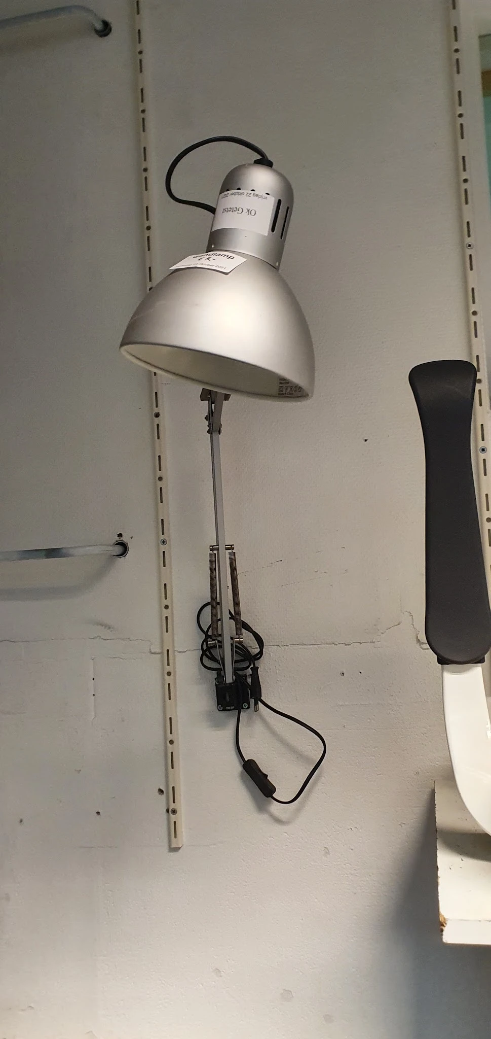 Staande lamp met witte kap en metalen standaard tegen witte muur