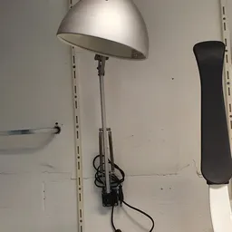 Staande lamp met witte kap en metalen standaard tegen witte muur
