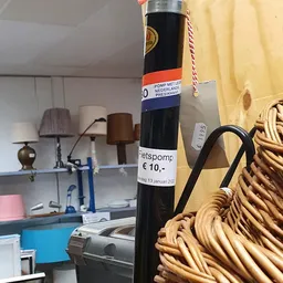 Close-up van een decoratieve zwarte fles met Nederlands etiket en een stroparaplu, tegen achtergrond met lichten en huishoude