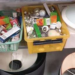 Gele opbergdoos met diverse huishoudelijke artikelen en onderdelen, zoals lampen, schakelaars en kleine spullen
