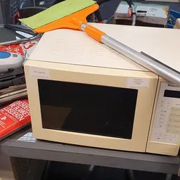 Vintage OKi Datasu magnetron met oranje handvat op werkblad tussen ander gebruikte huishoudapparatuur
