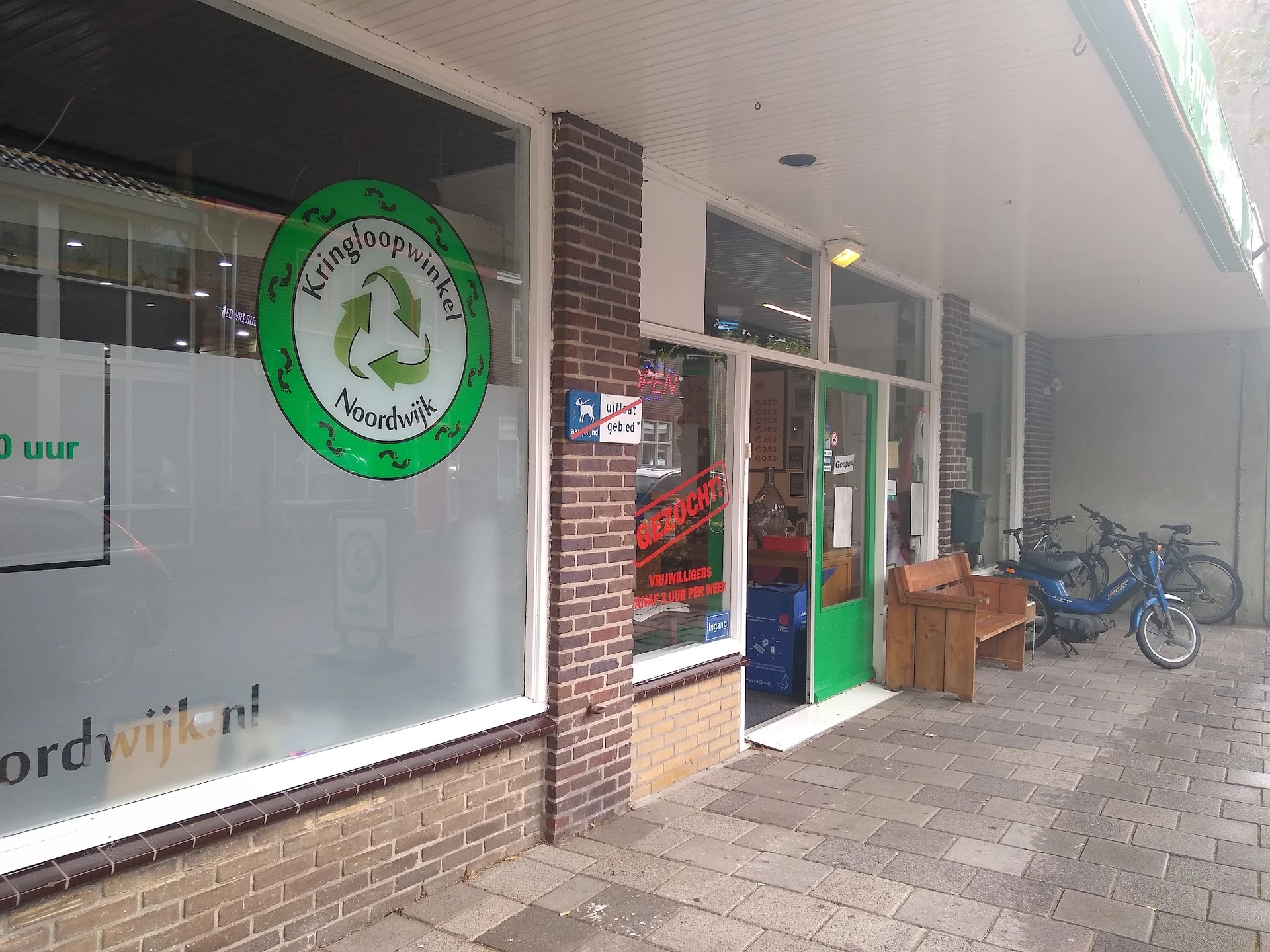 Winkelfront met groene deur, bakstenen gevel en groot groen rond logo met recyclesymbool