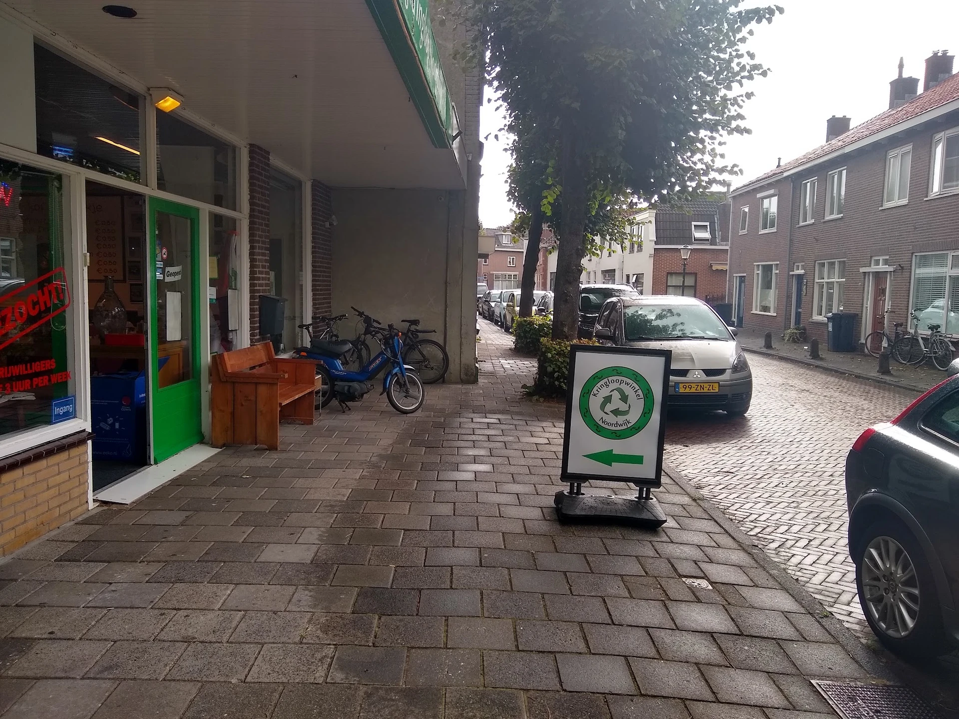 Straatview met kringloopwinkel, groene deur, fietsen en auto's geparkeerd