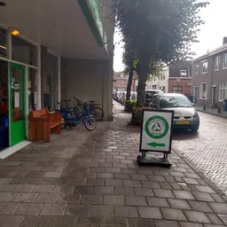 Straatview met kringloopwinkel, groene deur, fietsen en auto's geparkeerd