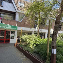 Gevel van kringloopwinkel met groene letters, rode deuren en houten plantenbakken ervoor