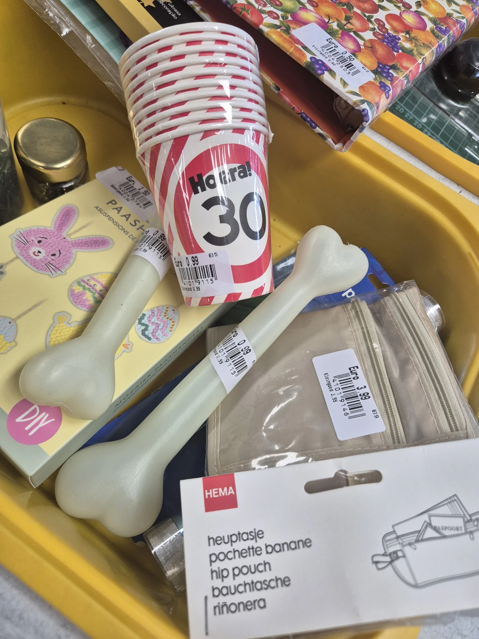 Gele plastic bakje met paarse bloemen, zonnebrandcrème SPF 30, witte voorwerp en verpakte items in plastic zak