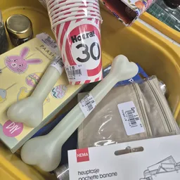 Gele plastic bakje met paarse bloemen, zonnebrandcrème SPF 30, witte voorwerp en verpakte items in plastic zak