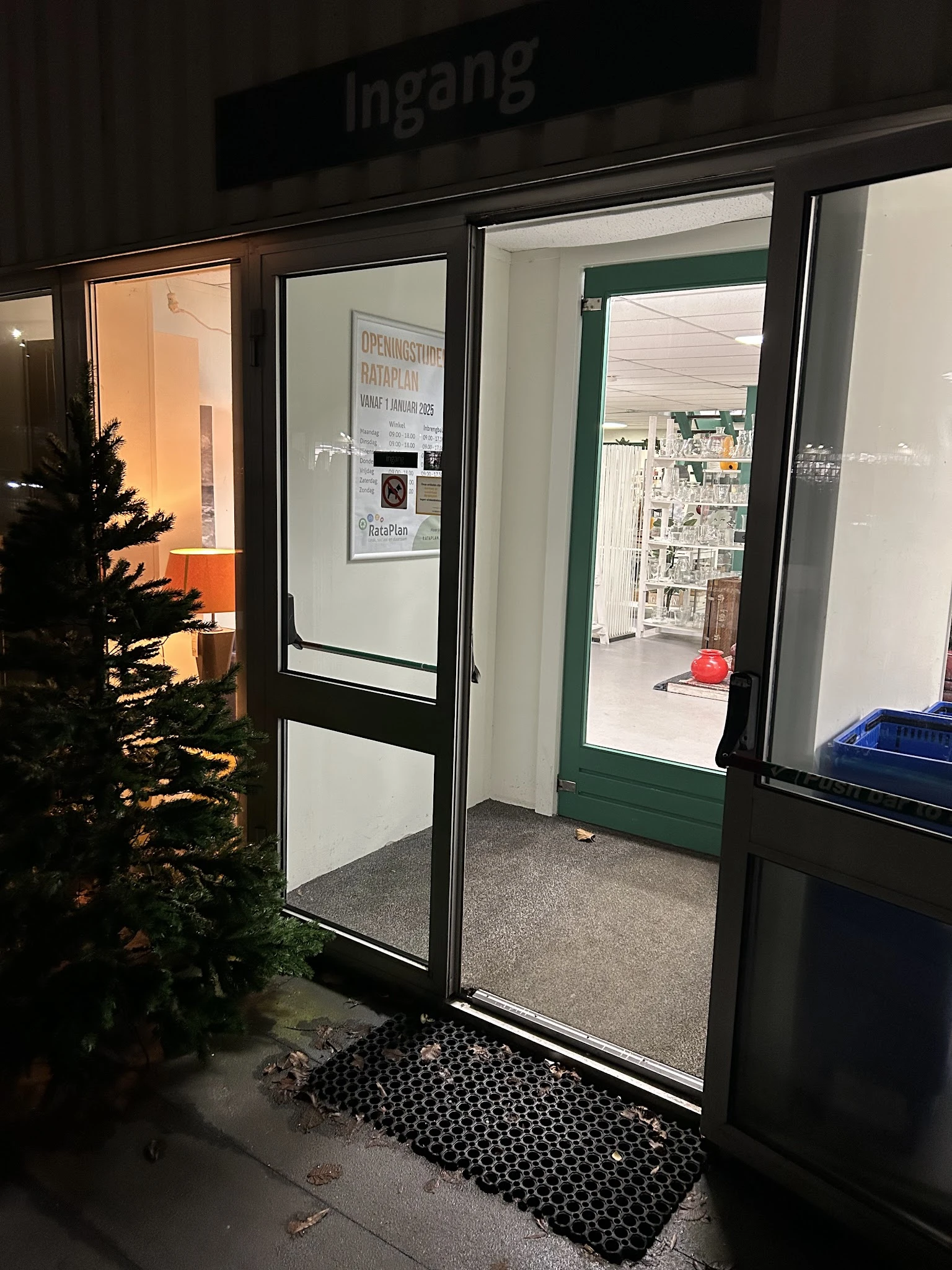 Winkelentree met glazen deuren, links kerstdecoratie, zicht op winkelruimte met stellingen