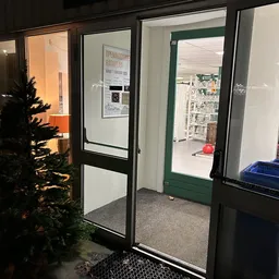 Winkelentree met glazen deuren, links kerstdecoratie, zicht op winkelruimte met stellingen