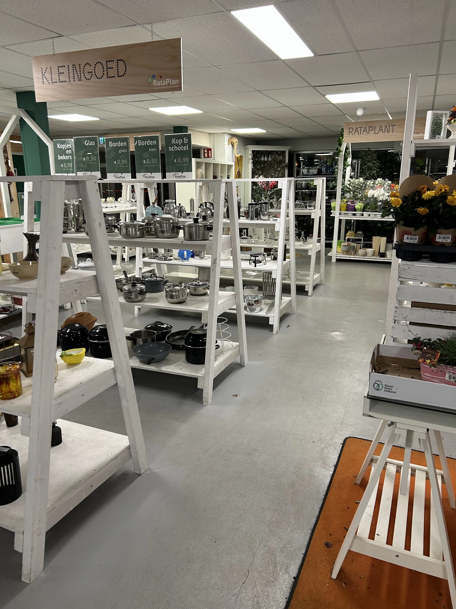 Winkelvloer met witte stellingen vol huishoudelijke artikelen, servies en keukengerei