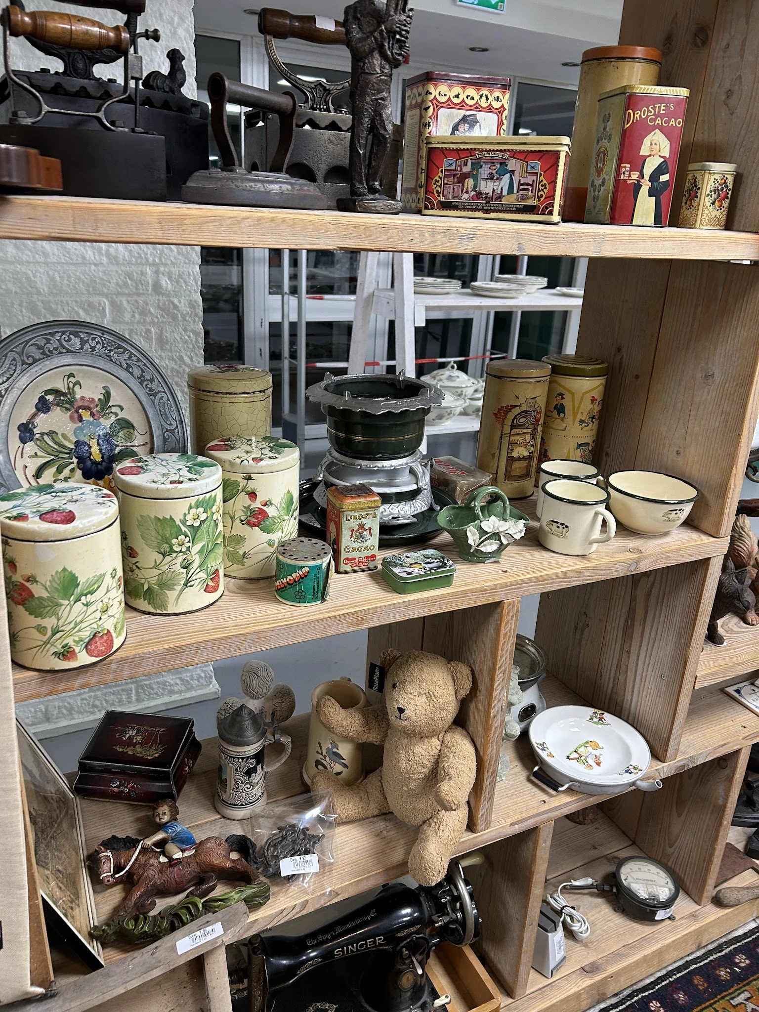 Houten stellingkast met verzameling vintage huishoudartikelen: bloemmotief blikken, keramische potten, kopjes en decoratieve 